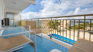 A balcony with a pool, lounge chairs, and a view of the sea.
