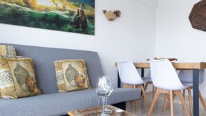 A modern living room with a grey sofa, two white chairs, a wooden coffee table, and a painting of a seascape.