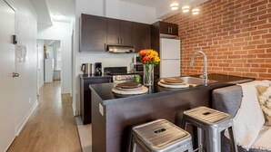 A compact kitchen with a brick wall, a stove, a sink, and a small dining area with stools.