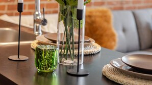 A kitchen counter with a vase of flowers, a candle holder, and a green glass.