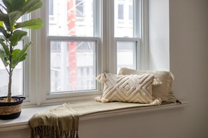 Un coin fenêtre aménagé avec une plante, des coussins et un plaid.