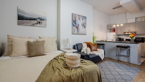A modern apartment with a bed, a sofa, a kitchen area, and a dining table.