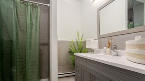 A modern bathroom with a shower curtain, a sink with a mirror, and a potted plant.
