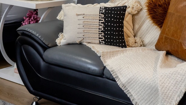 A black leather sofa with a white throw blanket and multiple pillows.