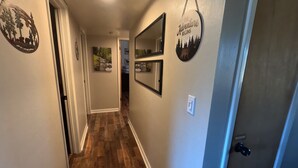 A hallway with wooden flooring, a door with a black handle, and wall decorations including a circular sign with the text "THE Adventure BEGINS".