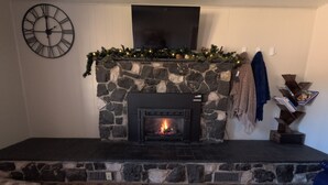 A stone fireplace with a fire, a clock on the wall, and a mantel decorated with greenery.