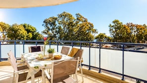 Un balcon avec une table dressée pour deux personnes, des chaises, un vase avec une fleur et un panier de fruits.