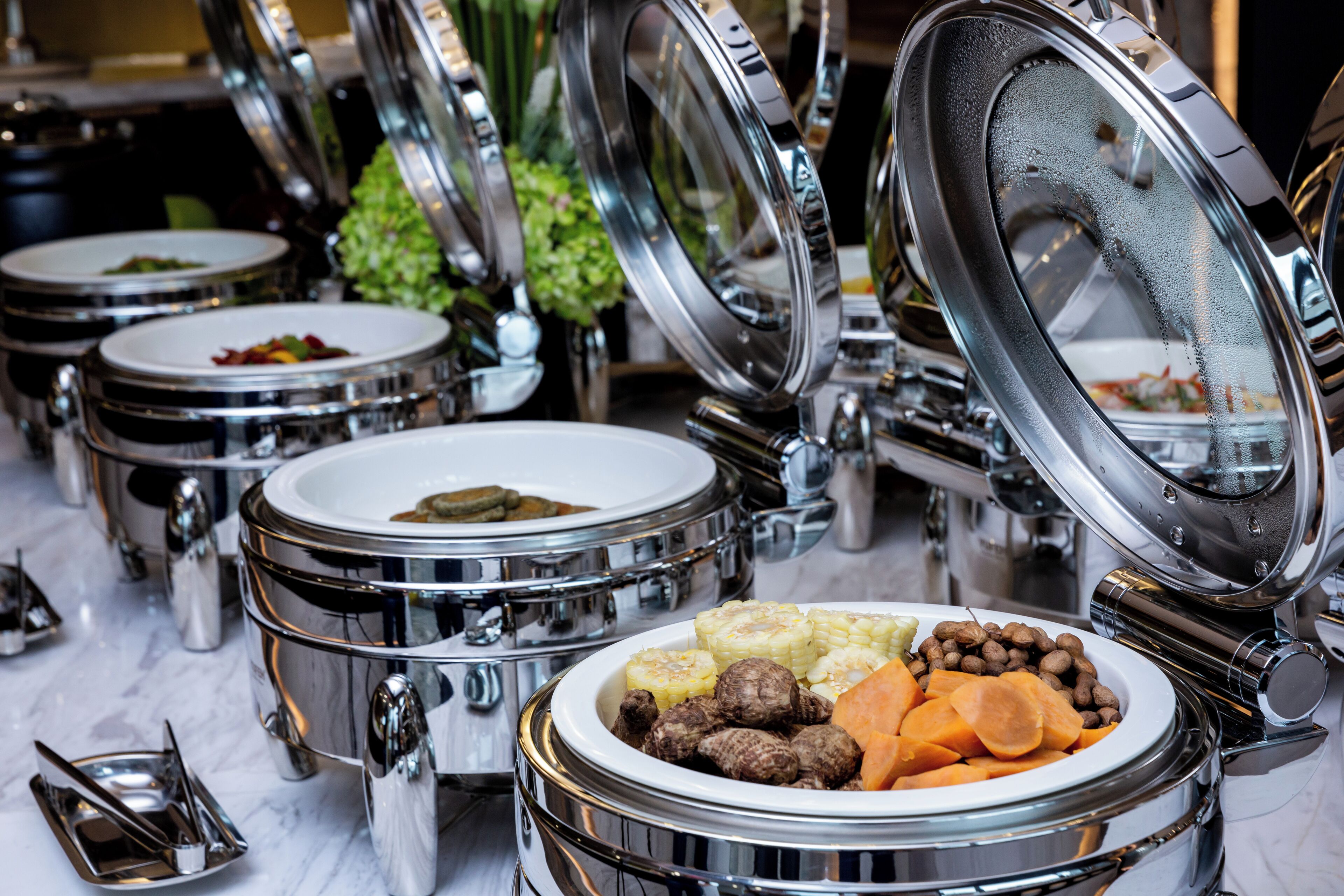 A buffet setup with multiple stainless steel chafing dishes, some with food visible.