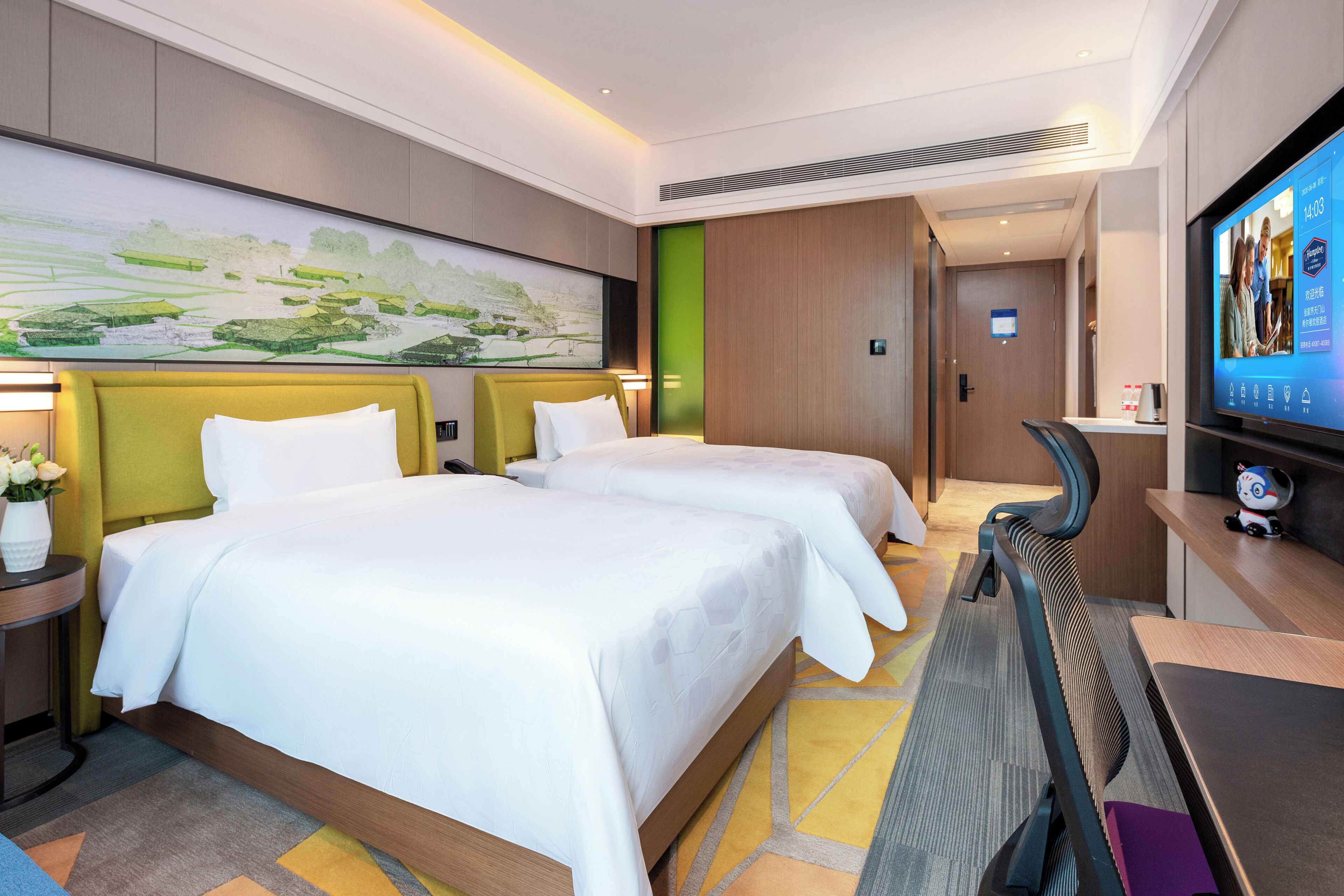 Ein Hotelzimmer mit zwei Betten, einem großen Flachbildfernseher, einem Laufband und einem Bild an der Wand.
