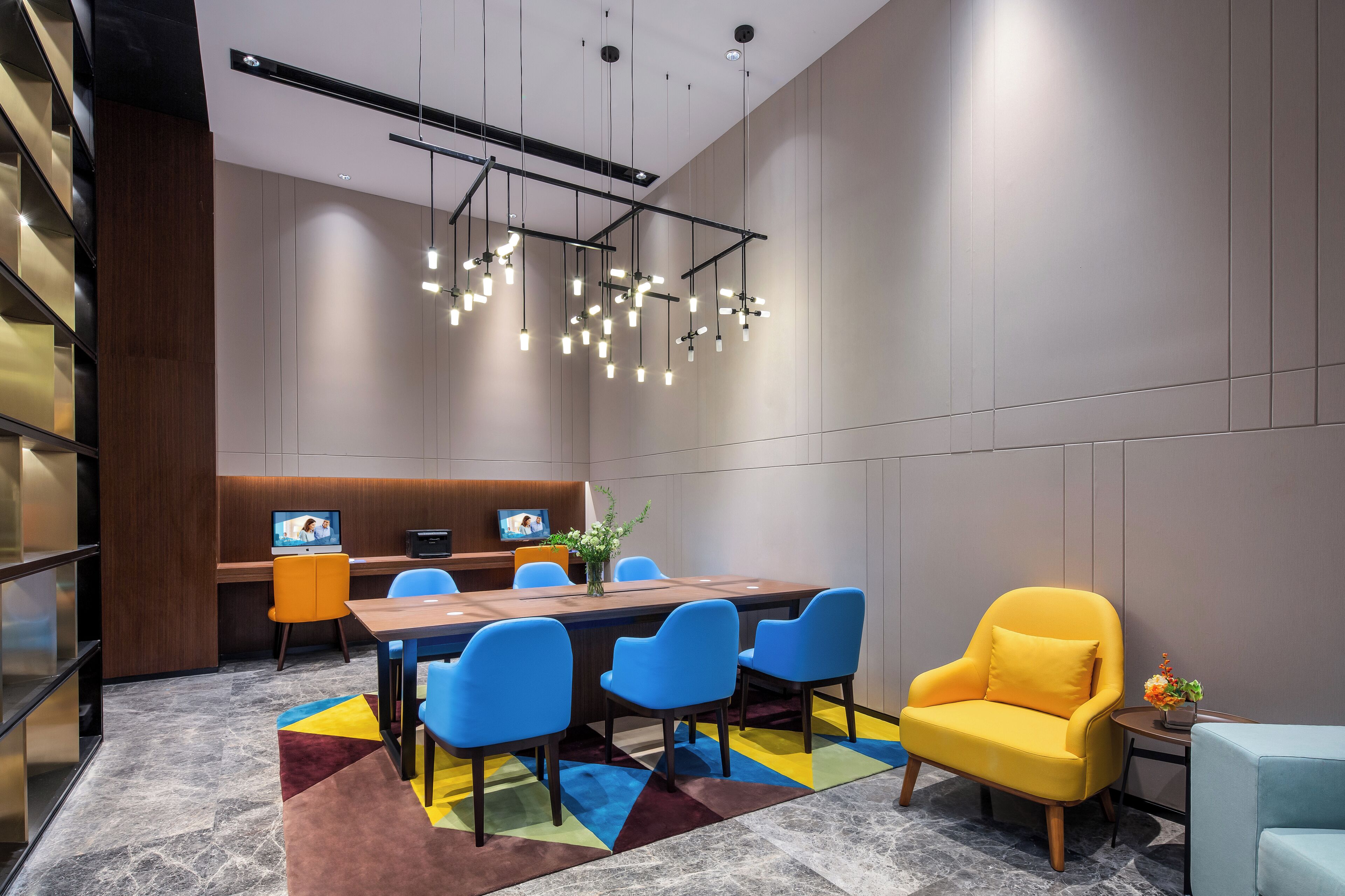 Une salle de conférence moderne avec une longue table, des chaises bleues, un fauteuil jaune et un écran de télévision.
