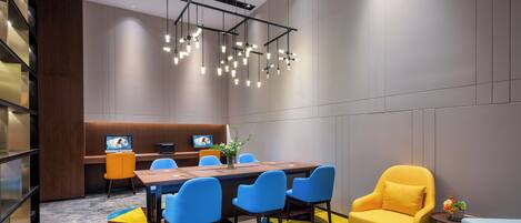 A modern conference room with a long table, blue chairs, a yellow armchair, and a TV screen.