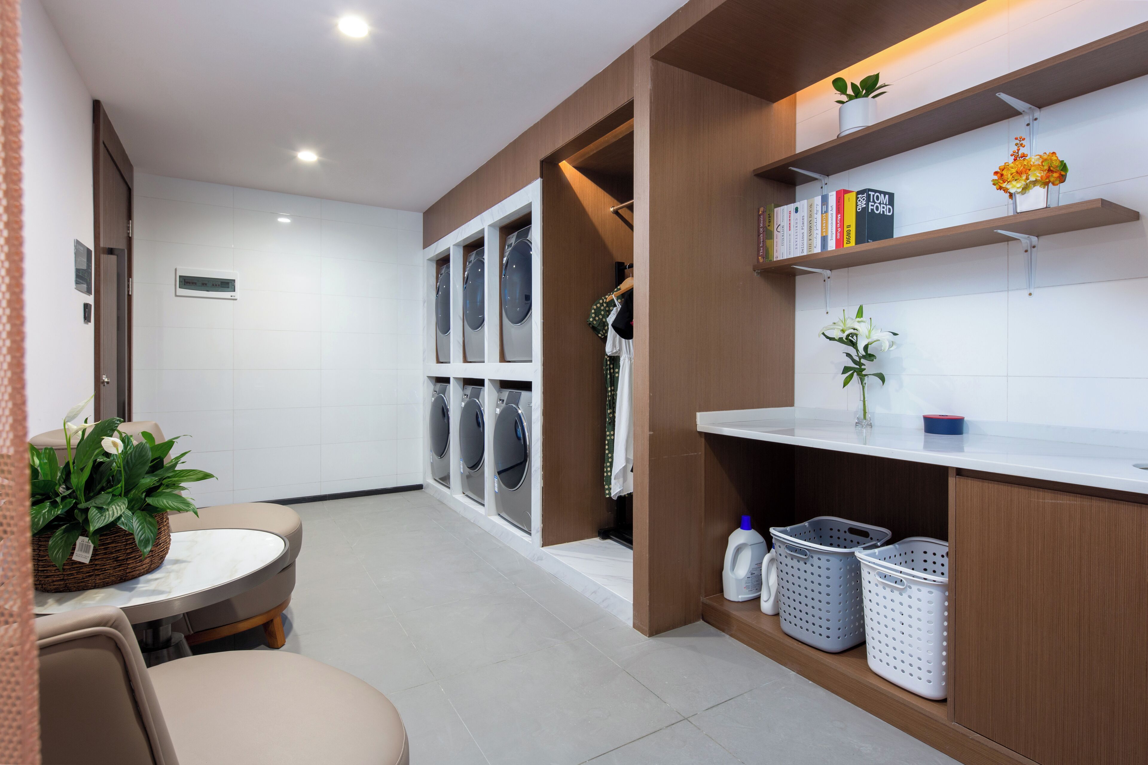 A modern laundry room with a washing machine, dryer, and shelves with books and decorative items.