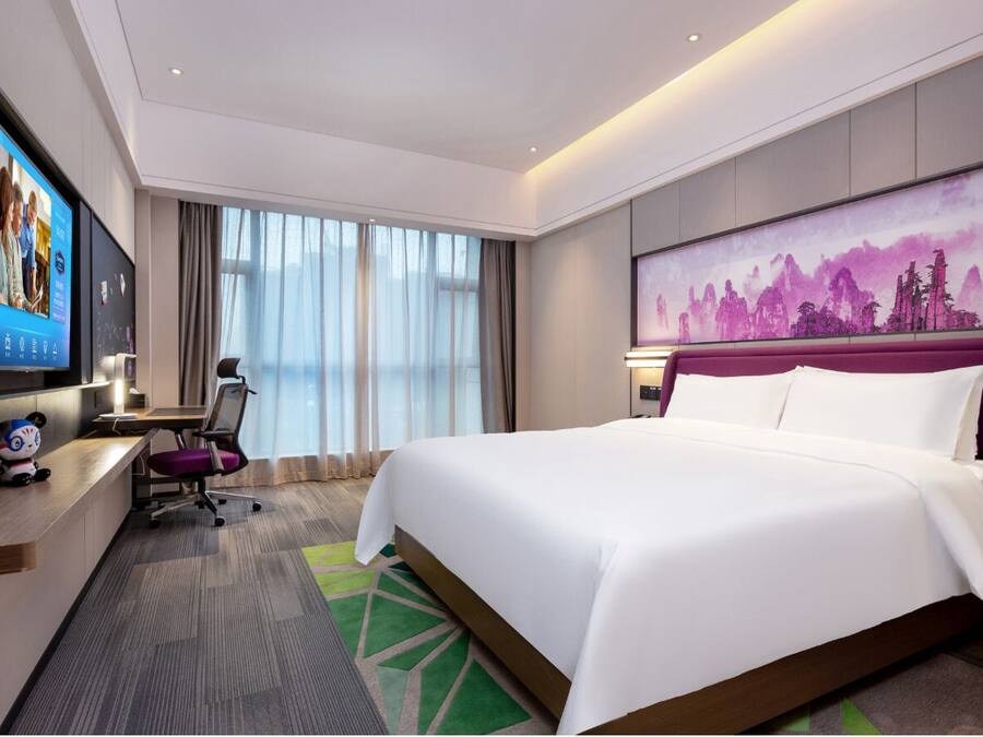 Una habitación de hotel con una cama grande, un escritorio con computadora, televisión y un cuadro en la pared.