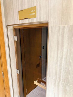 Une porte en bois sur laquelle est affiché un panneau indiquant « SAUNA » en arabe et en anglais.