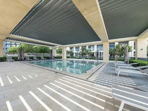Una piscina coperta moderna con area relax, sedie a sdraio e pavimento piastrellato.