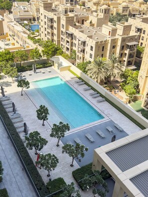 A rooftop swimming pool with sun loungers and trees, surrounded by apartment buildings.