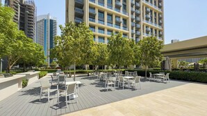 Un patio exterior con mobiliario y árboles, rodeado de edificios altos.