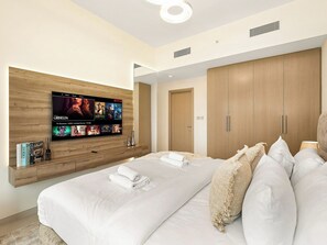 A modern hotel room with a large bed, a flat-screen TV mounted on the wall, wooden wardrobe, and a bedside table with a lamp.