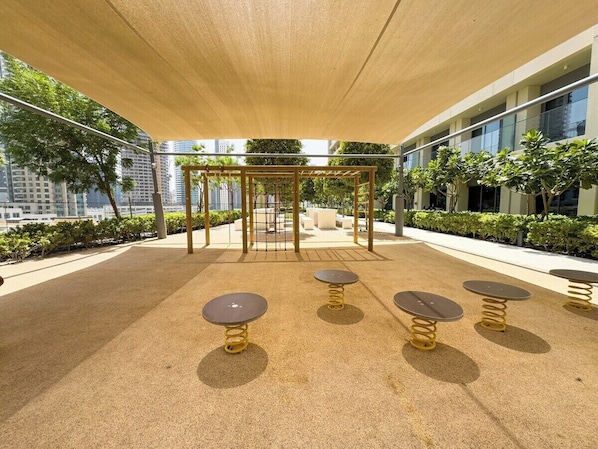 An outdoor seating area with tables and chairs, a pergola, and a view of the cityscape.