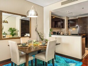A modern dining area with a wooden table, white chairs, and a blue rug. - Anantara Sea & Burj Al Arab View / Private Beach (Dubai)