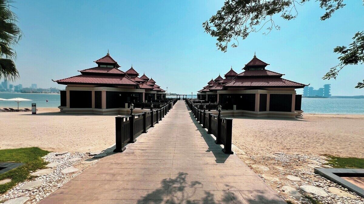 Een pad dat leidt naar traditionele paviljoens met uitzicht op het water en gebouwen in de verte.