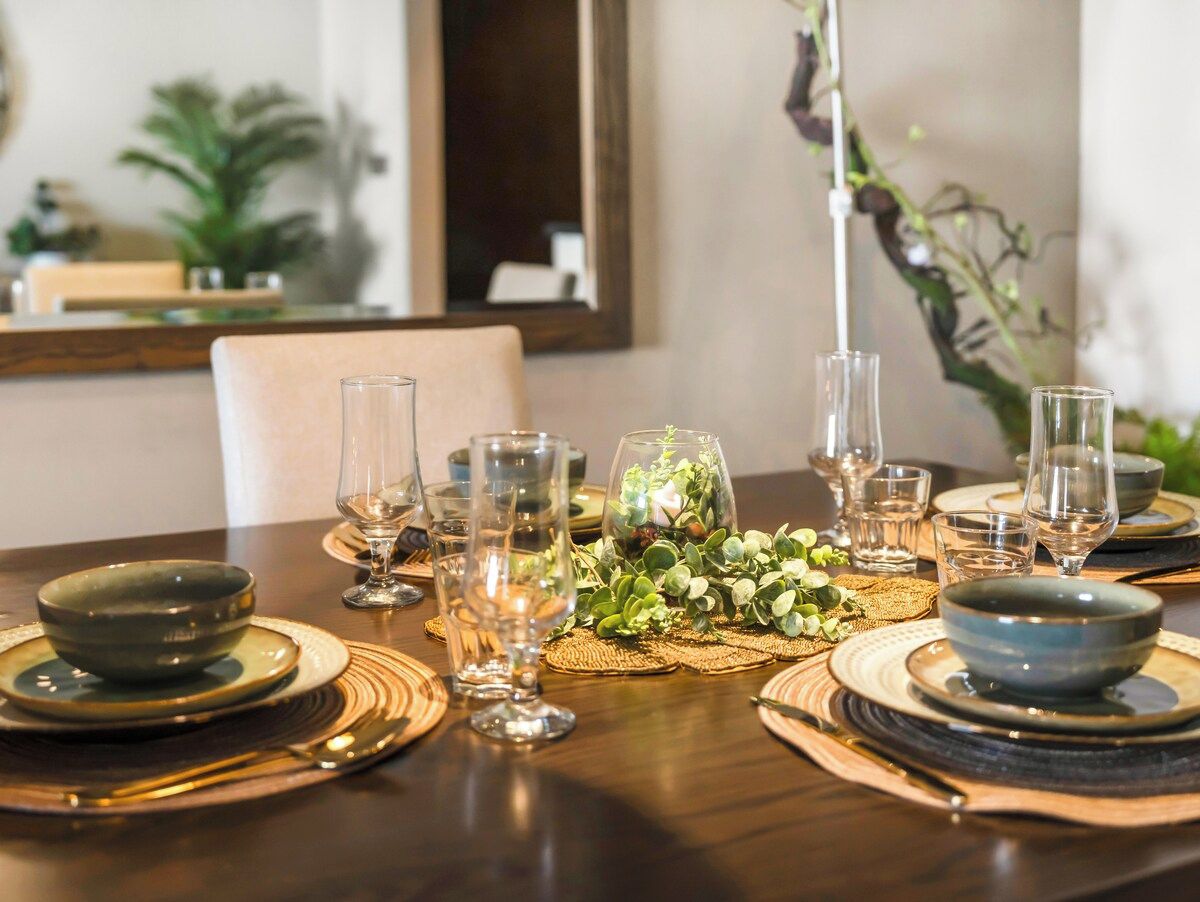 Een eettafel gedekt met diverse kommen, glazen en een middelpuntstuk met planten.