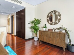 A modern living room with a wooden floor, a large potted plant, a wooden cabinet, and a decorative mirror on the wall.
