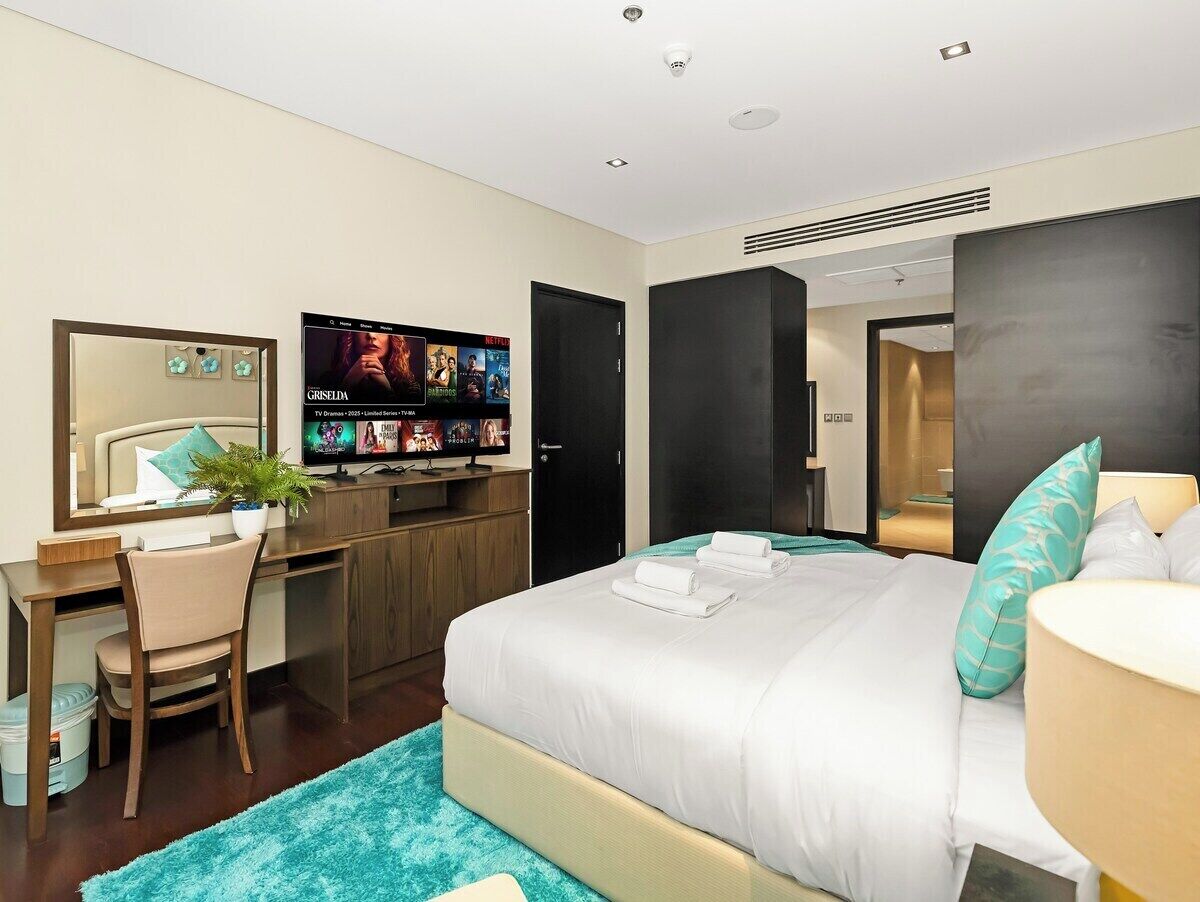 Quarto de hotel com cama, escrivaninha, televisão e espelho.