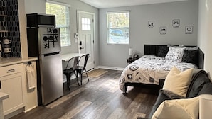 A compact bedroom with a bed, a desk, and a kitchenette. - The Level Up Studio (Jacksonville)
