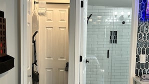 A modern bathroom with a glass shower enclosure, a white door, and a tiled floor. - The Level Up Studio (Jacksonville)