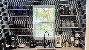 A kitchen with a black and white hexagonal tile backsplash, a window with blinds, and various kitchen items on the counter. - The Level Up Studio (Jacksonville)