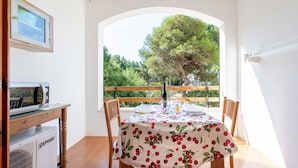 Un coin repas avec une table dressée pour deux personnes, un petit réfrigérateur et une fenêtre donnant sur les arbres.