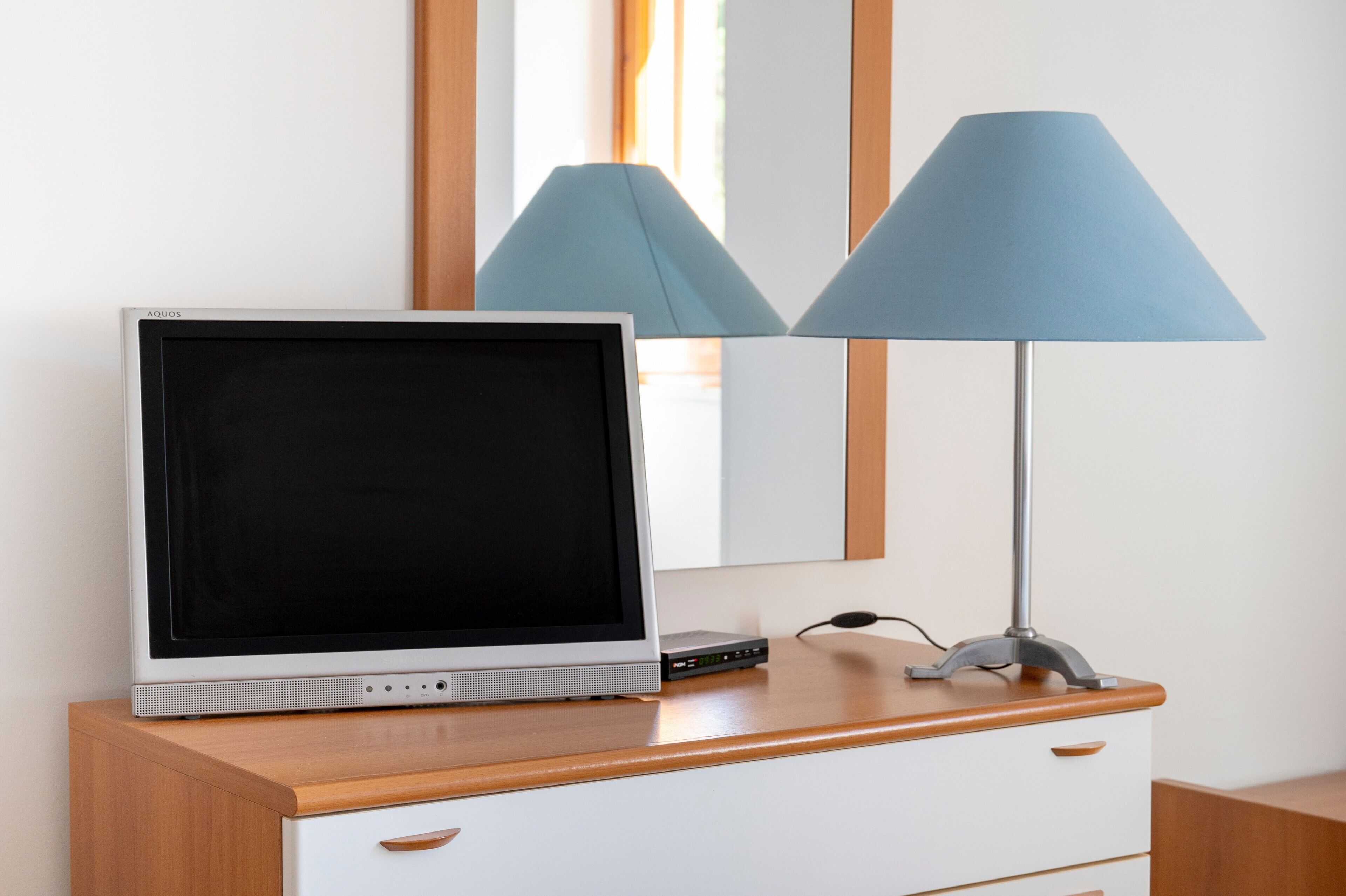 Ein Fernseher auf einem Holztisch, im Hintergrund eine Lampe und ein Spiegel.
