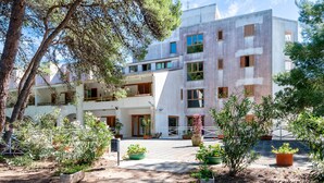 Un immeuble à plusieurs étages doté de balcons, de plantes en pot et d’une cour dallée.