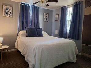 A hotel room with a bed, a ceiling fan, and a window with curtains.