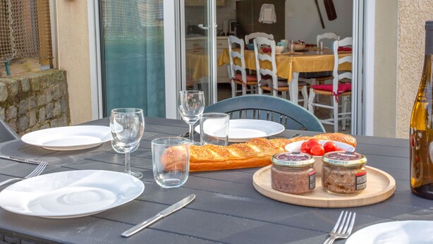 Une table dressée pour un repas, avec des assiettes, des verres, une baguette, des tomates et des pots de pâte à tartiner.