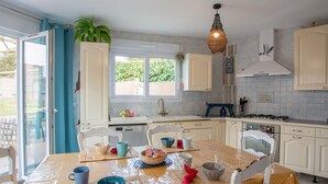Une cuisine avec des meubles blancs, une table à manger avec des chaises, un évier et une cuisinière.