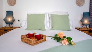 Un lit bien fait, agrémenté d’oreillers verts, un panier contenant des tasses rouges et une pâtisserie, et deux lampes fixées au mur.
