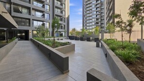 Un patio urbano moderno con techo plano, jardineras de hormigón y una variedad de árboles y arbustos.