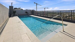 Una piscina en la azotea con vistas a la ciudad y grúas de construcción al fondo.