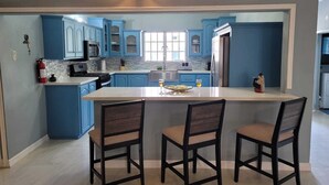 A modern kitchen with blue cabinets, a central island with chairs, and a built-in microwave. - Villa Flores- New Modern Luxury Villa within walking distance from ANR Airport. (Bon Accord)