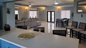 A modern kitchen with a central island, dining area with chairs, and a living room with a sofa and TV. - Villa Flores- New Modern Luxury Villa within walking distance from ANR Airport. (Bon Accord)