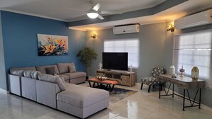 A modern living room with a sectional sofa, a flat-screen TV, a dining table with chairs, and decorative items. - Villa Flores- New Modern Luxury Villa within walking distance from ANR Airport. (Bon Accord)