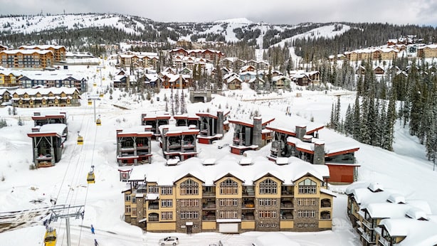 Un complejo turístico cubierto de nieve con varios edificios, telesillas y montañas al fondo.
