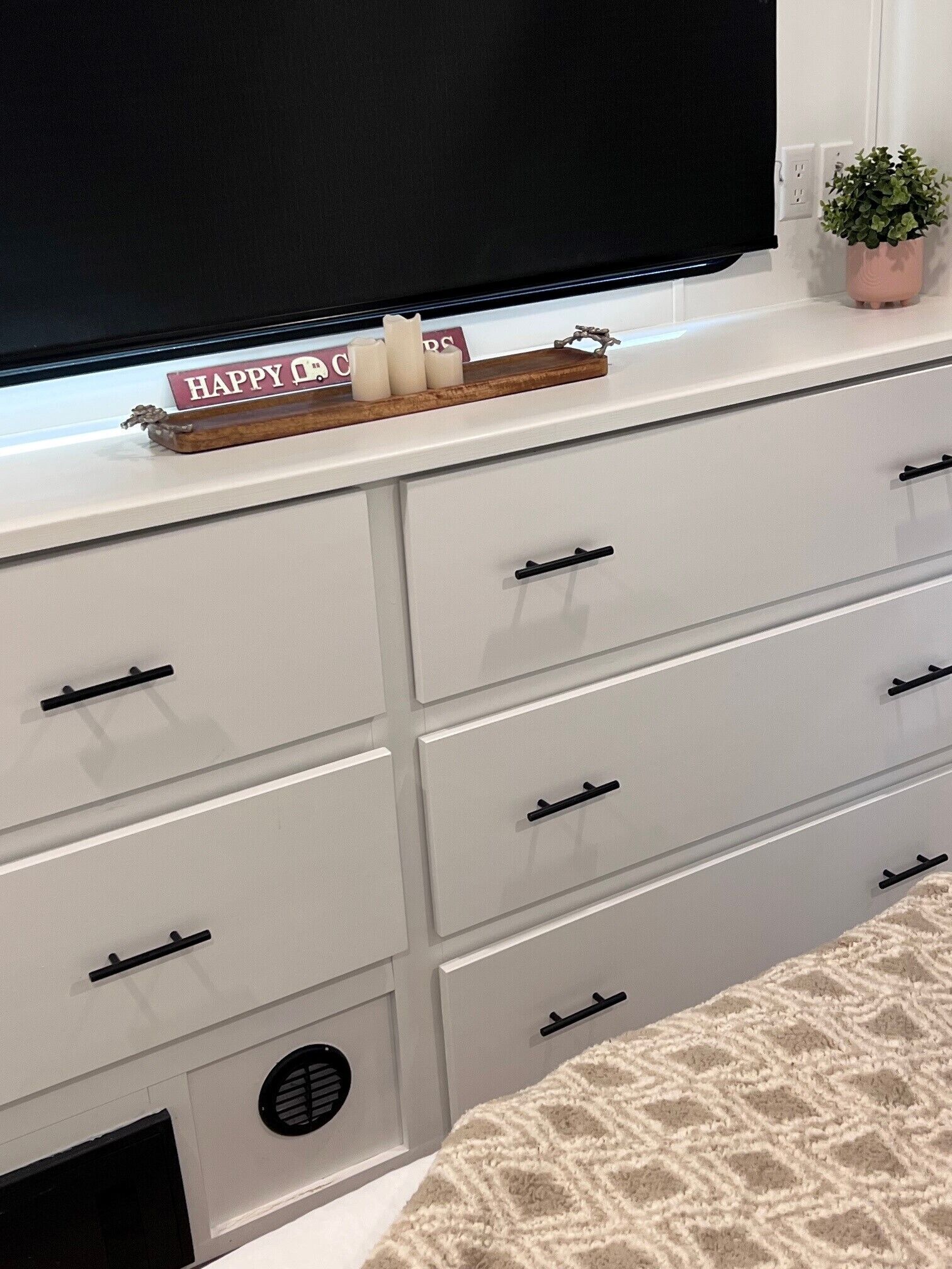 Un aparador blanco con varios cajones y un televisor de pantalla plana montado encima.