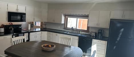 A kitchen with white cabinets, a black refrigerator, a microwave, and a wooden dining table with chairs.