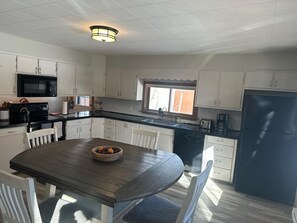 A kitchen with white cabinets, a black refrigerator, a microwave, and a wooden dining table with chairs. - Tranquil Yampa Getaway (Yampa)