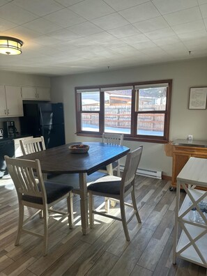 Een eetgedeelte met een donker houten tafel en witte stoelen, een zwarte koelkast en een raam met uitzicht op een traditioneel gebouw.