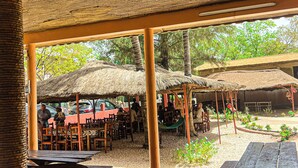 An outdoor dining area with thatched-roof structures, wooden tables, and chairs. - Hôtel Finio (Joal-Fadiout)