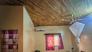 A room with a bed, a chair, a window with curtains, a ceiling fan, and a mosquito net. - Hôtel Finio (Joal-Fadiout)